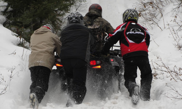 A group of people push an ATV in the snow