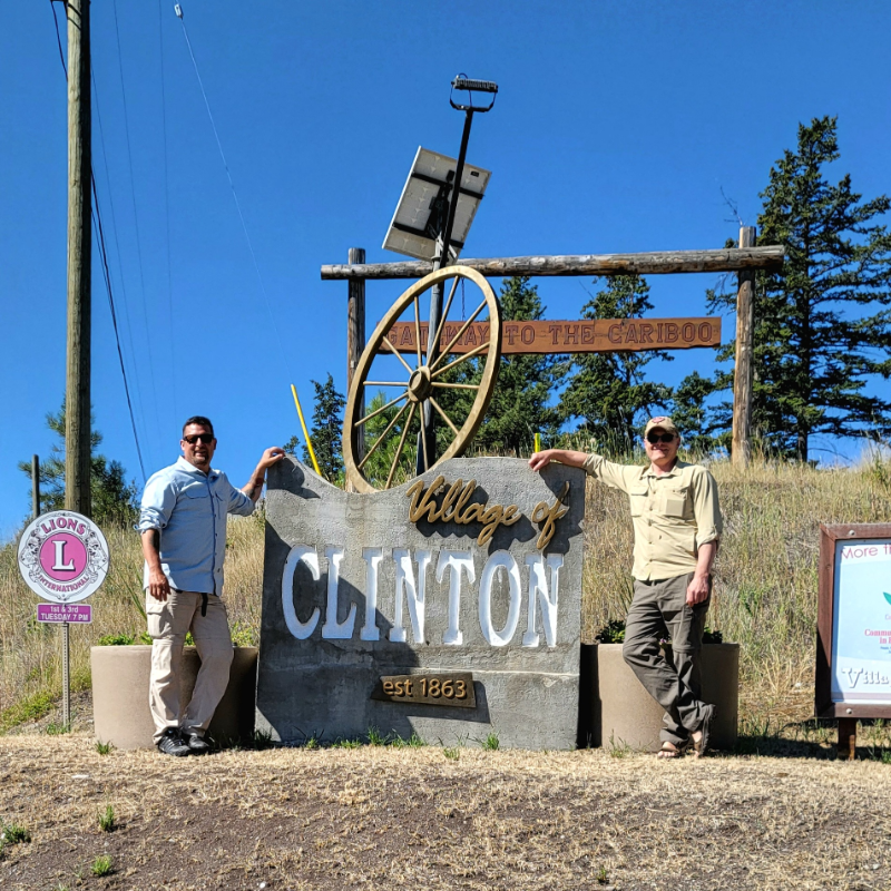 John Giannisis and his friend, Antony Francis, pose in from a sign that says Village of Clinton.