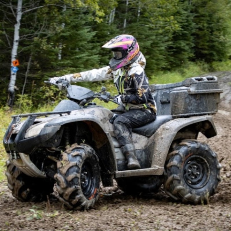 A woman rides an ATV through a muddy trail in the forest. 