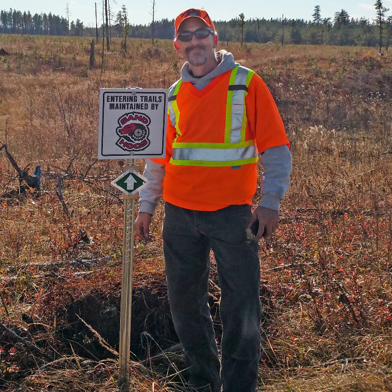 Gary Hora wears an orange and yellow reflective vest while smiling and standing in a field. 