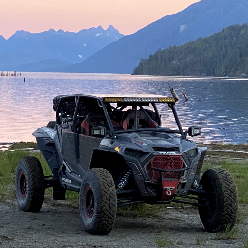 Two side-by-side ATVs next to a lake at dusk with a pink sunset over mountains in the background. 