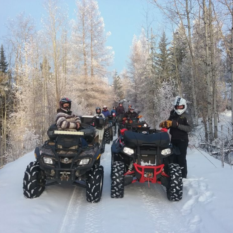 A row of ATVs ride next to each other on a snowy trail. 