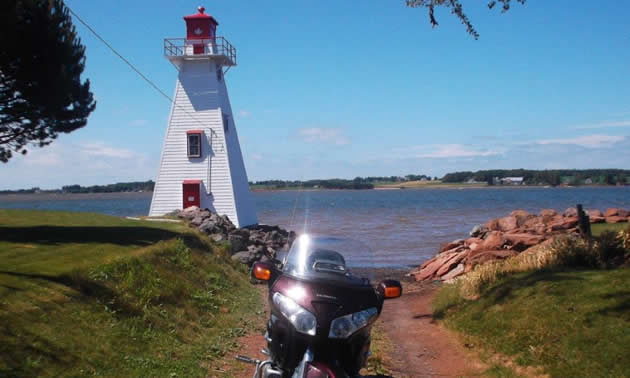 A motorcycle parked by a red and white lighthouse. 