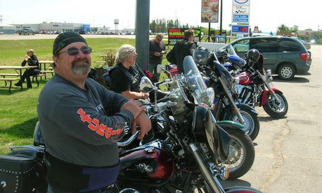 A line up of bikers stopped at a gas station.