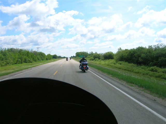 A photo taken from behind a bikers windshield, looking at two bikes on the highway in front of it.