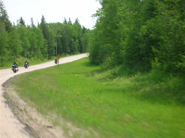A photo of a curve in the road and three bikes on the highway off in the distance.