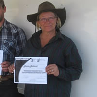 A woman in and a man smile and hold up certificates while a man in a white shirt stands next to them.