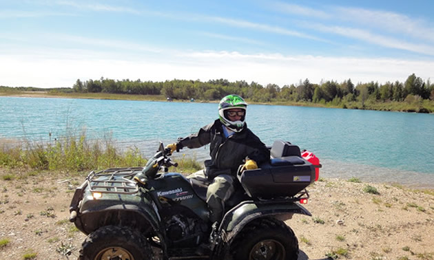 a man standing beside an ATV in front of a lake