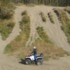 A ATV rider sits at the bottom of a dune looking up at the trails and the blue sky.