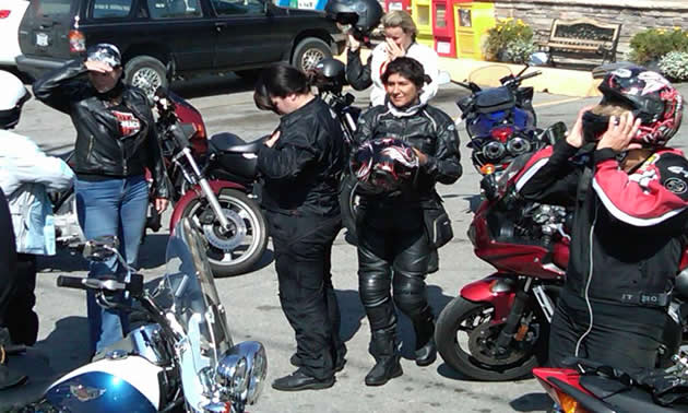 women in motorcycle garb mingle around their parked bikes.