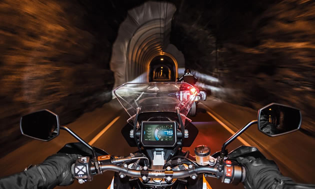 Picture from driver's perspective, showing dashboard of bike, and driving through dark tunnel. 