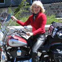 Middle-aged blond woman sits astride a Harley Davidson motorcycle