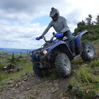 Someone on a blue ATV descends down a steep shale slope while a group looks on.