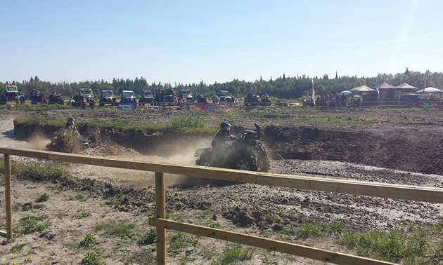 Two ATVs race on a muddy track.