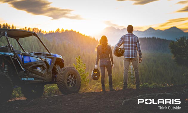 Two people standing side-by-side, looking at sunset, with ATV beside them. 