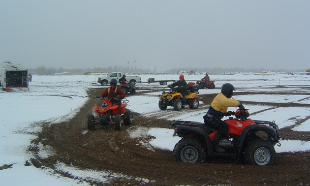 Group of people riding ATVs in snowy field, practicing manoeuvres. 