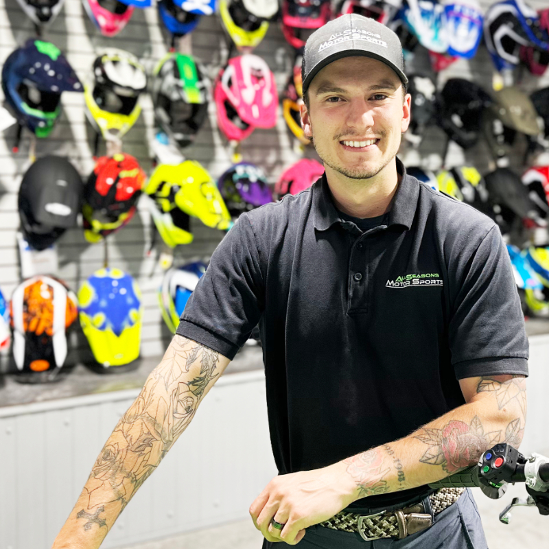 Dayton Pouliot with his arm on a bike handle with helmets in the background at All Seasons Motorsports