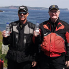 Photo of two men holding up a water bottle filled with seawater. They are standing in front of an ocean. 