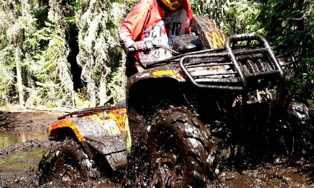 An ATV tearing through deep mud. 