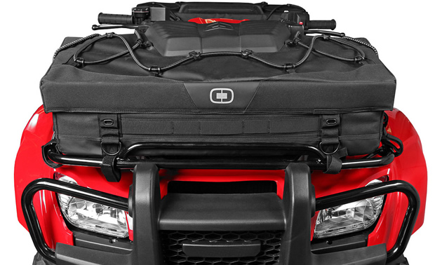 The front of a red ATV with a black bag strapped to the rack of it. 
