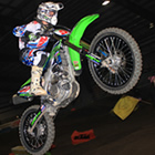 A young man going over a jump on a neon green dirt bike.
