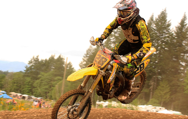 A young man landing a yellow dirt bike over a jump. 