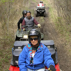 A lady in a blue jacket riding a red quad is in front of two other ATVs riding on a grassy trail. 