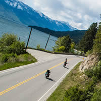 Two motorcyclists travelling down a road along a lake. 