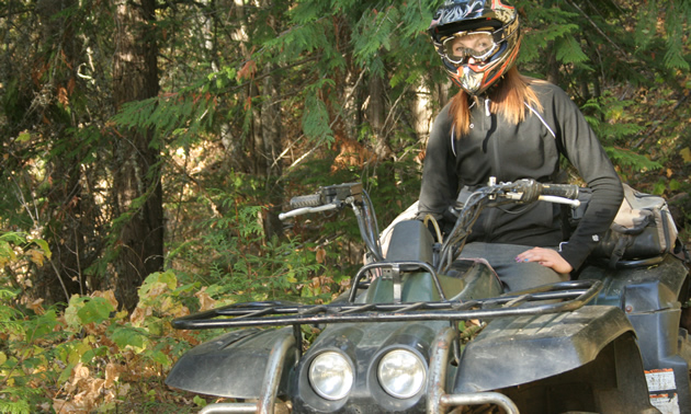 A young woman with brown hair sitting on a green ATV. 