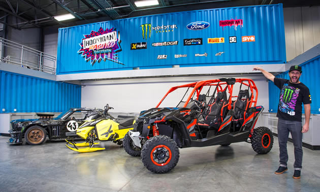 Ken Block standing beside his red and black Can-Am side-by-side. 