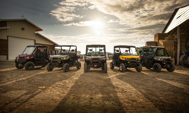 Five of Can-Am's new Defender utility side-by-sides lined up in a farmyard. 