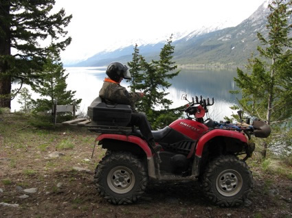 An ATVer sits on the back of a quad in front of a mountain lake
