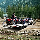 People driving trucks loaded with ATVs near a woodland area