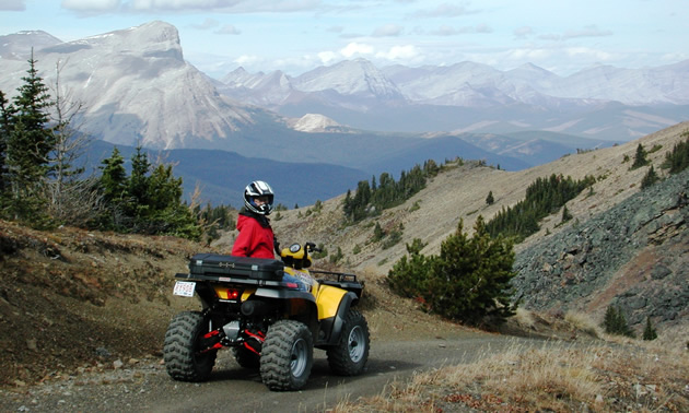 Riders come from near and far to experience the amazing beauty of Southern Alberta's backcountry. Shown is an ATVer parked with the Rocky Mountains in the background.