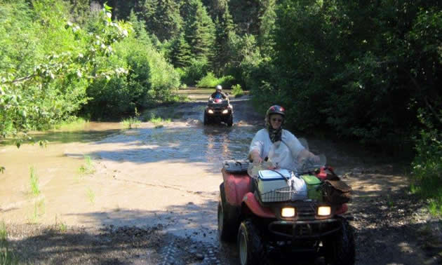 A woman on an ATV riding through a mud puddle. 