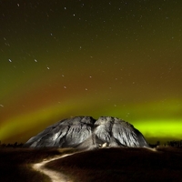 An amazing view of the the northern lights, stripes of yellow and green, over a small mountain. 