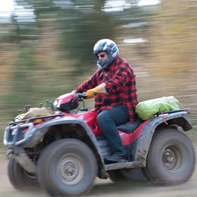 Man riding an ATV down dirt road.