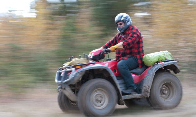 Man riding an ATV down dirt road.