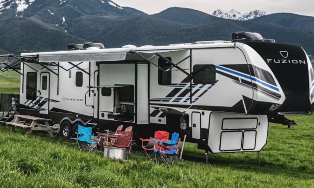 Two massive white RVs are parked with sun shining on the mountains in the distance