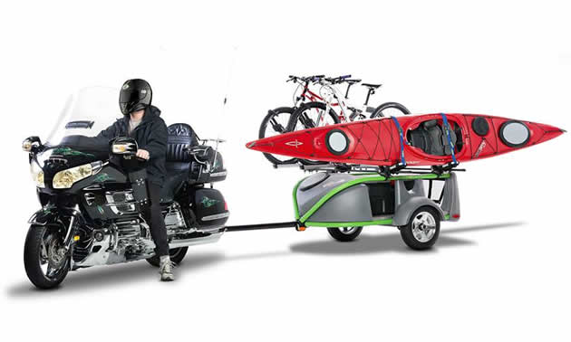 A black cruiser motorcycle towing a trailer with bikes and a kayak on it. 