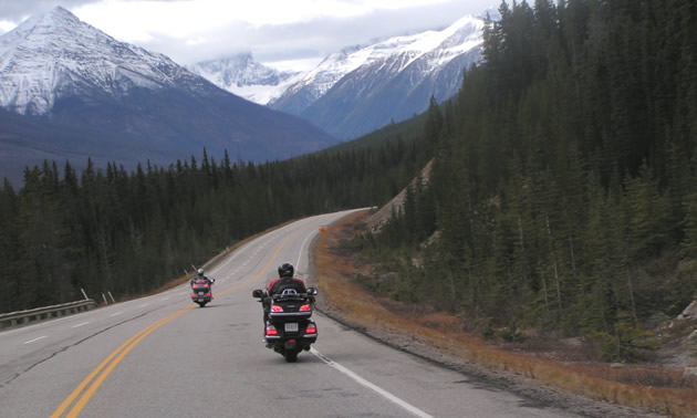 Two bikers riding through the mountains on a highway. 