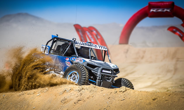 A Hellenbach Racing UTV is racing through desert sand.