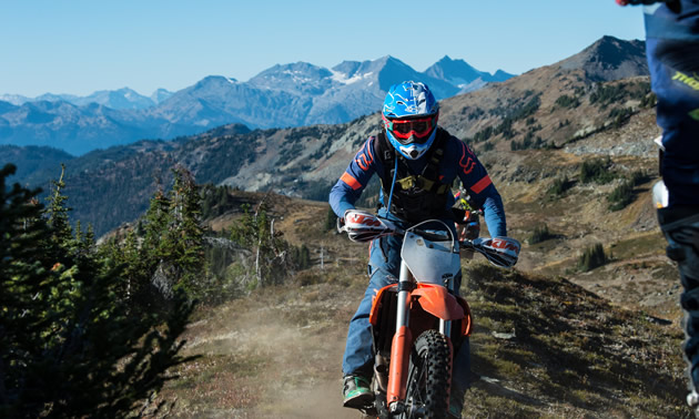A shot of Jason Ribi riding toward the camera and behind him is mountainous terrain. 