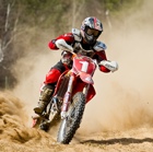 A guy riding around a turn on a dirt bike with dust billowing