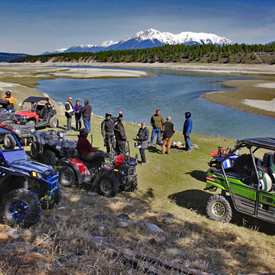 A group of ATVs and side-by-sides parked beside the Kootenay River. 