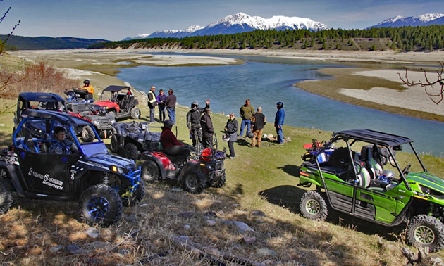 A group of ATVs and side-by-sides parked beside the Kootenay River. 