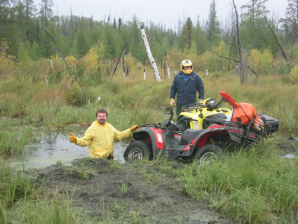 Man in mud waist deep next to a man standing by an ATV