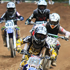 Photo of a group of young kids riding their dirt bikes down a dirt track towards the camera. 