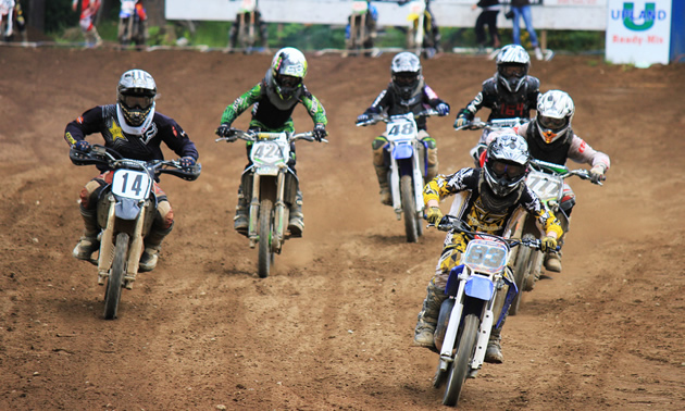 Photo of a group of young kids riding their dirt bikes down a dirt track towards the camera. 