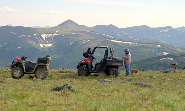 A RZR and a quad parked on a mountain meadow. 